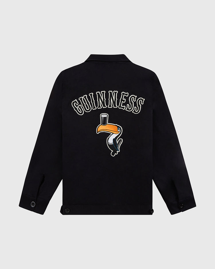 The Guinness Cotton Grounds Crew Jacket by Ebbets Field features “Guinness” in bold white letters above an embroidered toucan balancing a pint on its beak, displayed from the back against a plain light background.