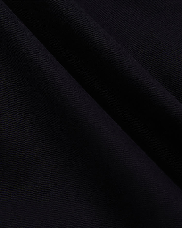 Close-up of the Guinness Cotton Grounds Crew Jacket by Ebbets Field, showing dark, folded cotton fabric with a smooth texture and subtle diagonal lines, which create gentle shadows and highlights on the material.