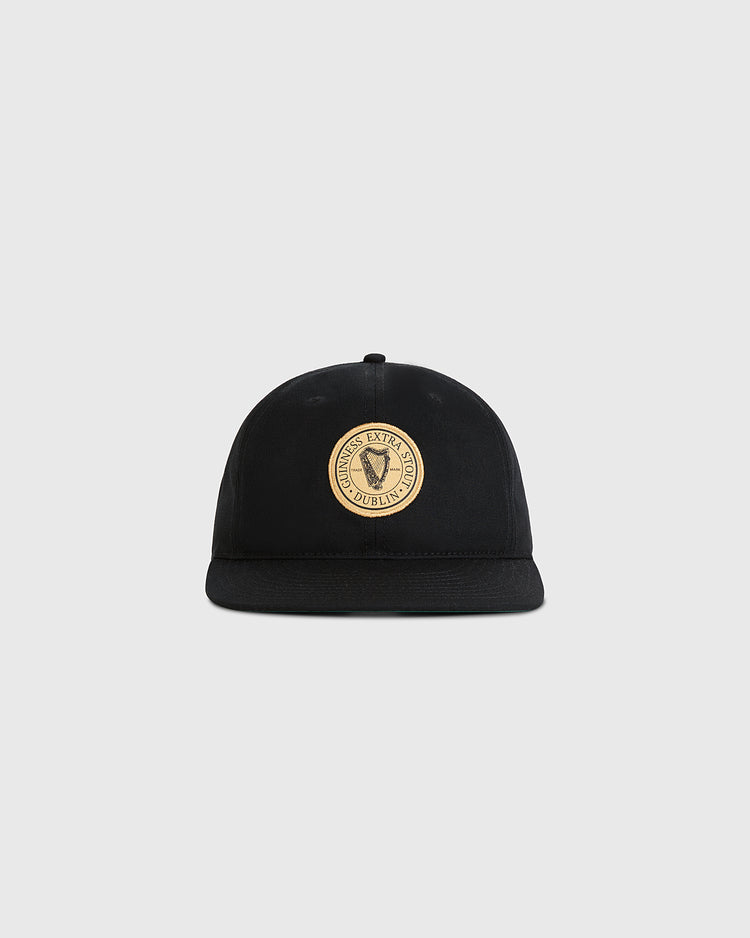 The Ebbets Field Guinness Extra Stout Badge Cotton Twill Ballcap features a black design with a round beige patch reading Dublin Excise on the front, displayed against a plain light gray background.
