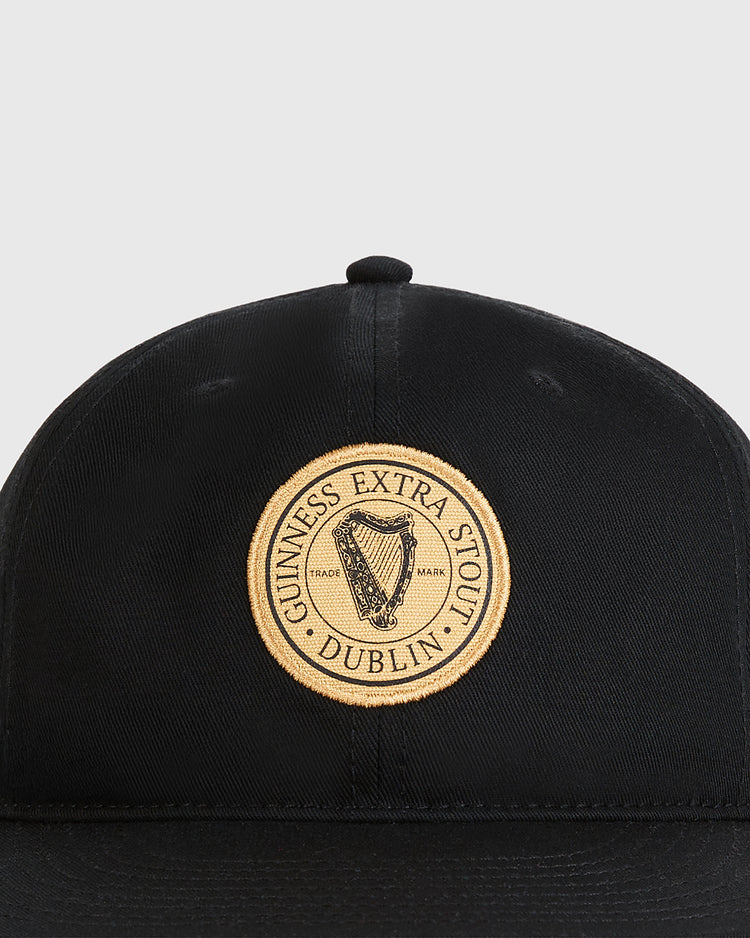 The Ebbets Field Guinness Extra Stout Badge Cotton Twill Ballcap is a black cap with a round gold patch reading 