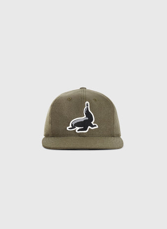 The Guinness Seal Authentic Wool Ballcap by Ebbets Field is a khaki green cap featuring a black and white seal balancing a ball patch on the front, shown against a plain white background.