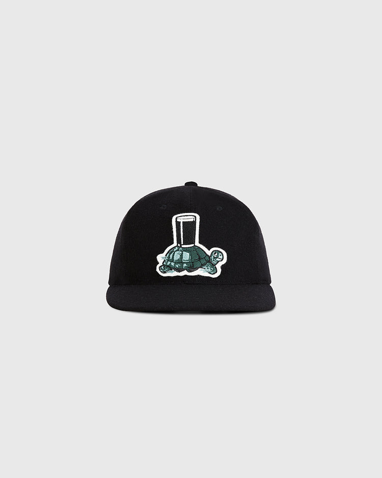 The Guinness Tortoise Authentic Wool Ballcap by Ebbets Field features an embroidered green turtle with a tall glass on its shell, centered on the front, displayed against a plain light gray background.