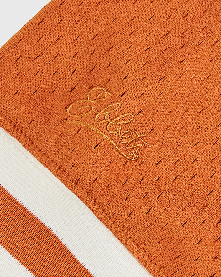 Close-up of orange mesh fabric with small holes and embroidered “Ebbets Field” script. Cream and orange striped edge is inspired by the University of Texas 1982 V-Neck Mesh Jersey worn at the College World Series.