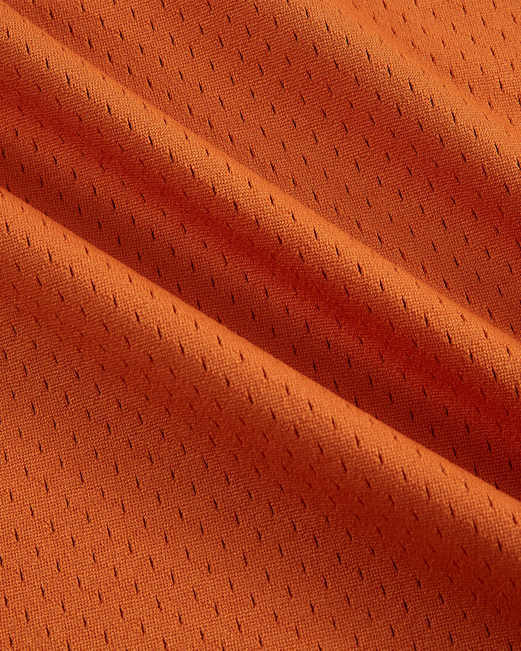 Close-up of the Ebbets Field University of Texas 1982 V-Neck Mesh Jersey fabric, highlighting orange mesh with small perforations, visible diagonal folds, and detailed stitching inspired by the original Longhorns jersey.