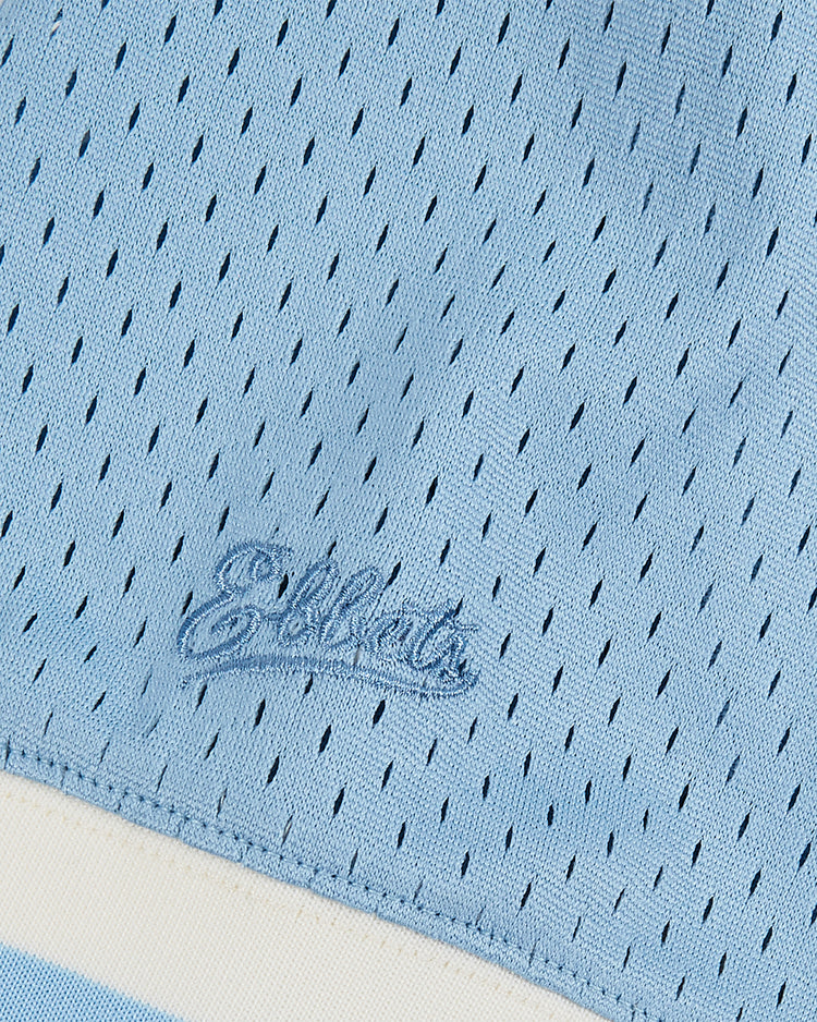 Close-up of the Ebbets Field Jackie Robinson Powder Blue V-Neck Mesh Jersey, featuring small holes, “Ebbets” script embroidery, and a cream stripe along the bottom edge—evoking classic baseball style.