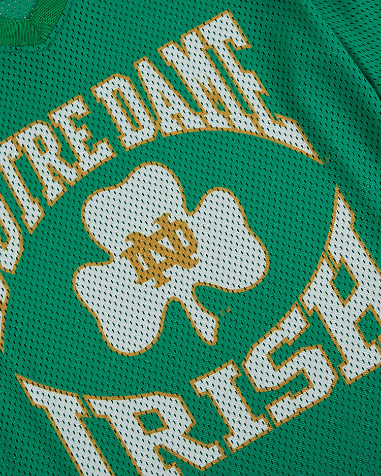 The Ebbets Field University of Notre Dame V-Neck Mesh Jersey is a green top with white and gold “Notre Dame Irish” text and a large shamrock with ND initials, inspired by vintage Notre Dame baseball style.