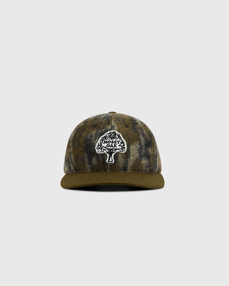 The Ebbets Field Mossy Oak x Ebbets Field Vintage Tree Logo Ballcap features a camouflage design, olive green brim, and black-and-white tree logo patch with “Mossy Oak” text. The cap is displayed centered on a plain light background.
