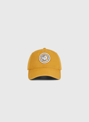 The Ebbets Field Hawaii Civic Auditorium Roller Rink Washed Cotton Ballcap in mustard yellow features a circular blue and white patch, inspired by the historic rink, shown against a plain light gray background.