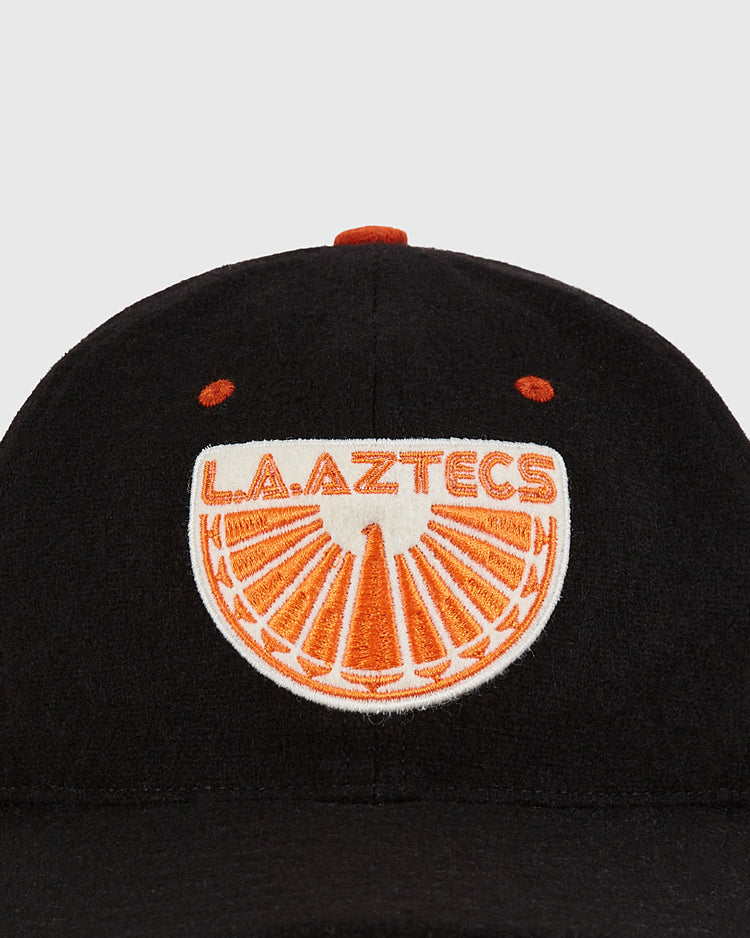 The Los Angeles Aztecs Wool Ballcap by Ebbets Field is a black cap featuring an orange and white embroidered L.A. AZTECS patch with a stylized orange segment design on the front.