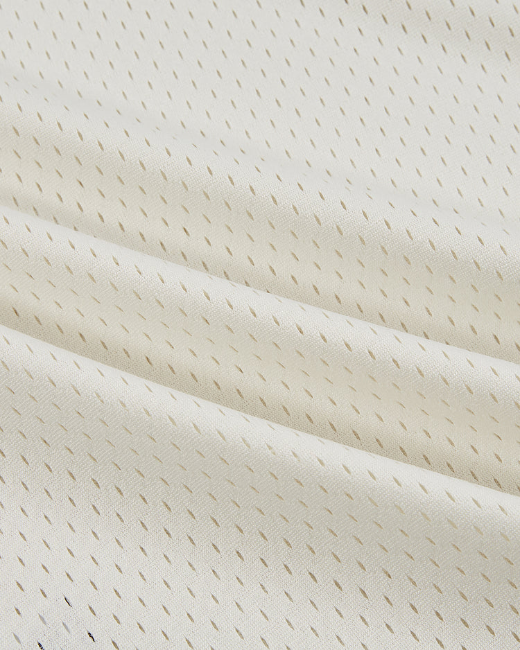 Close-up of the Ebbets Field Pennsylvania Stoners Mesh Soccer Jersey, cream-colored with small vertical perforations in a subtle textured pattern. The softly draped fabric shows gentle folds and shadows.
