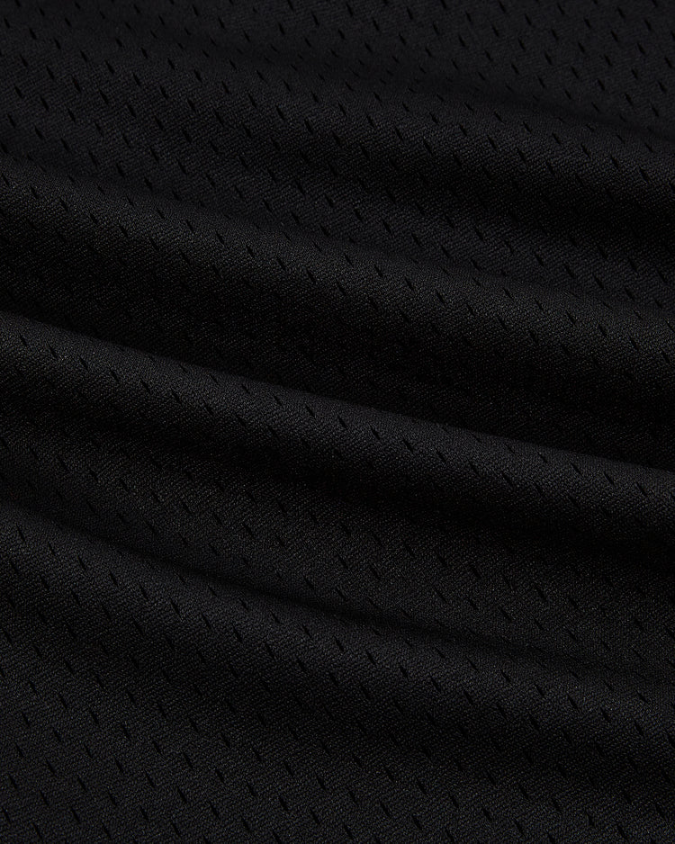 Close-up of black mesh fabric with small perforations and gentle folds, highlighting the texture and sheen of the Ebbets Field Los Angeles Aztecs Mesh Soccer Jersey.