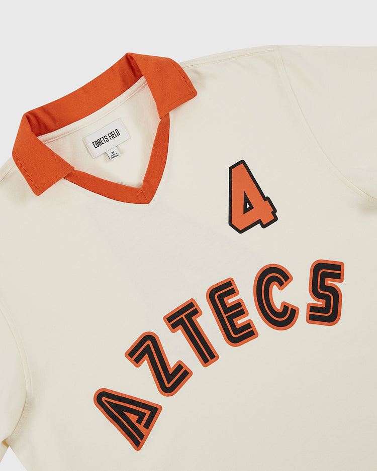 The Ebbets Field Los Angeles Aztecs Vintage Collar Soccer Jersey features a cream cotton body, orange collar, bold 