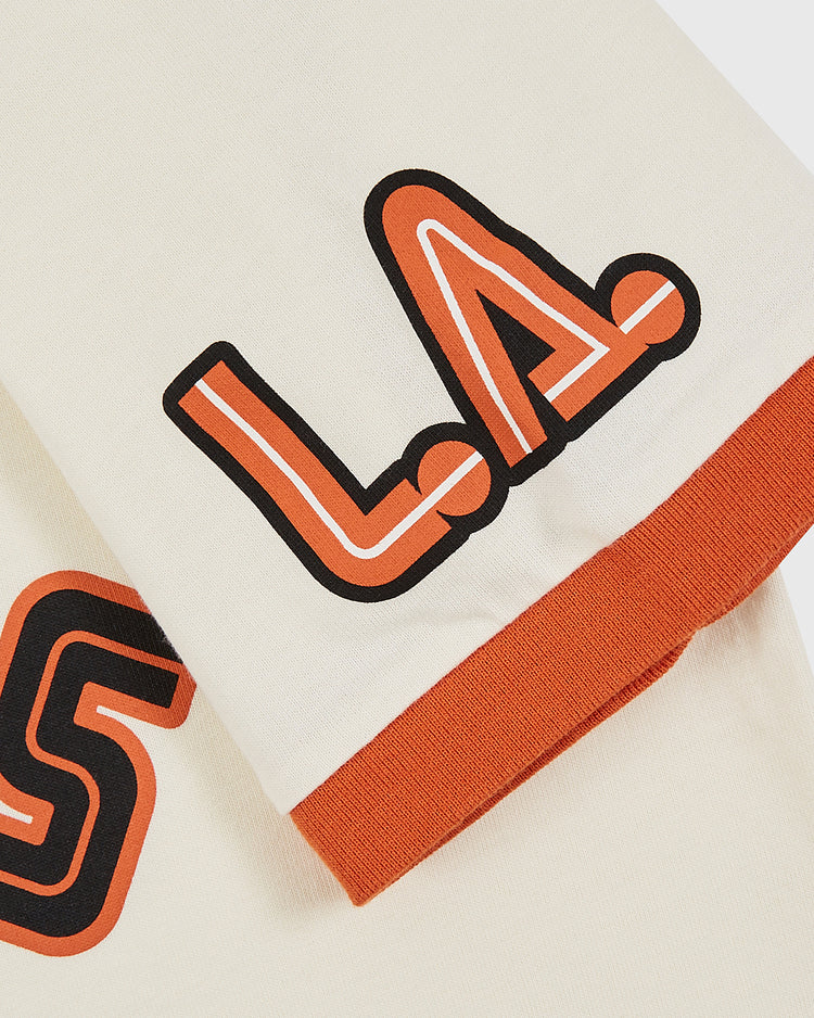 A close-up of Ebbets Field’s Los Angeles Aztecs Vintage Collar Soccer Jersey shows cream fabric with bold, orange and black outlined 