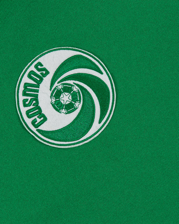 A close-up of the Ebbets Field New York Cosmos Vintage Soccer Goalie Jersey, a green collared long sleeve with an embroidered round “COSMOS” logo featuring a spinning motif and central soccer ball.