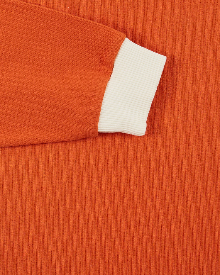 Close-up of the Los Angeles Aztecs Vintage Soccer Goalie Jersey by Ebbets Field—an orange long sleeve with a white ribbed cuff, laid flat on a matching orange background.