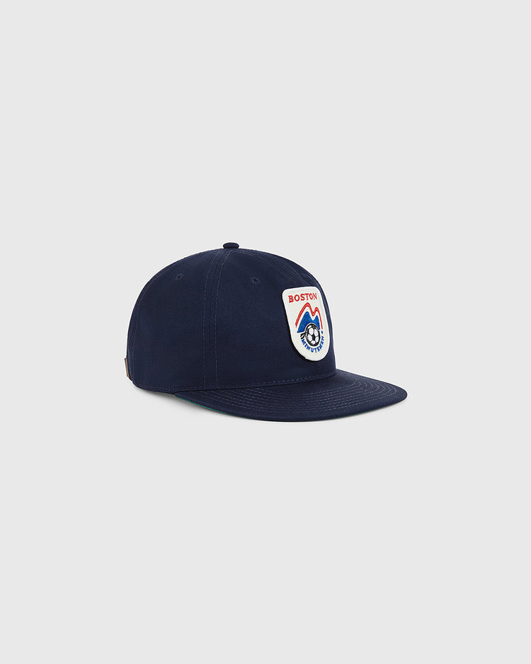 The Ebbets Field Boston Minutemen Cotton Twill Ballcap is navy blue with a colorful embroidered felt Boston logo patch featuring a mountain and wolf graphic, displayed on a plain light gray background.