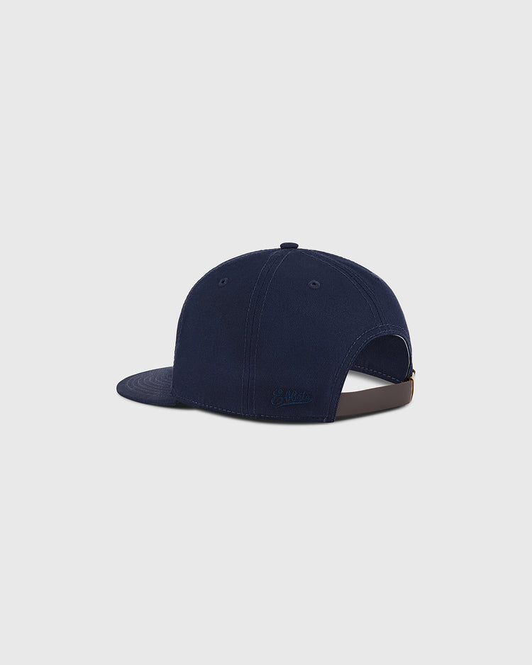 The Ebbets Field Boston Minutemen Cotton Twill Ballcap is shown from the back-left, featuring a navy blue design, curved brim, and adjustable brown strap with metal buckle against a plain light gray background.