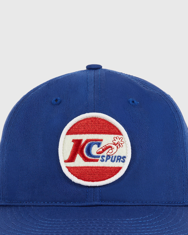 The Ebbets Field Kansas City Spurs Cotton Twill Ballcap features a circular patch with KC Spurs in red and blue on a white and red background, celebrating the legacy of the Kansas City Spurs’ NASL championship.