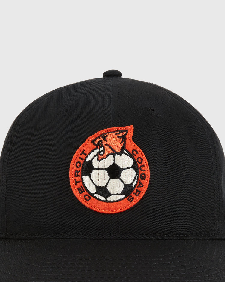 The Detroit Cougars Cotton Twill Ballcap by Ebbets Field is a black cap with a circular patch featuring a cougar, soccer ball, and 