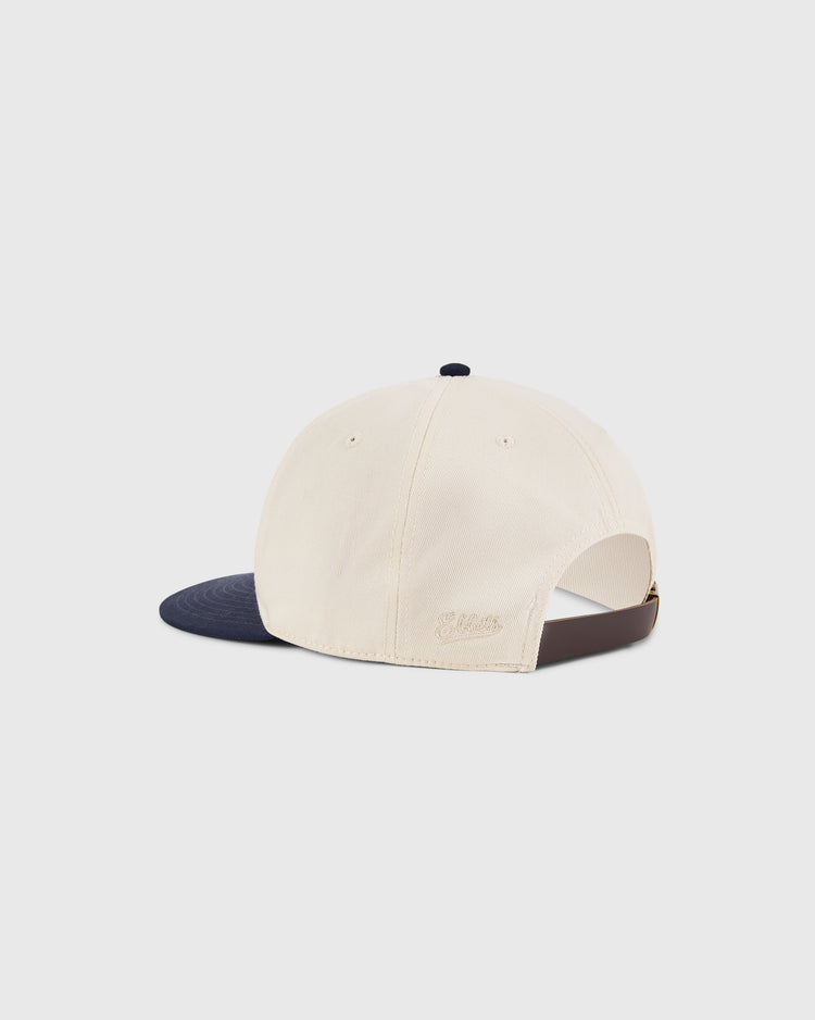 The Ebbets Field Sam Adams Crest Cotton Twill Ballcap is cream-colored with a navy brim, shown from the back. It features an adjustable strap and subtle embroidered text near the opening.