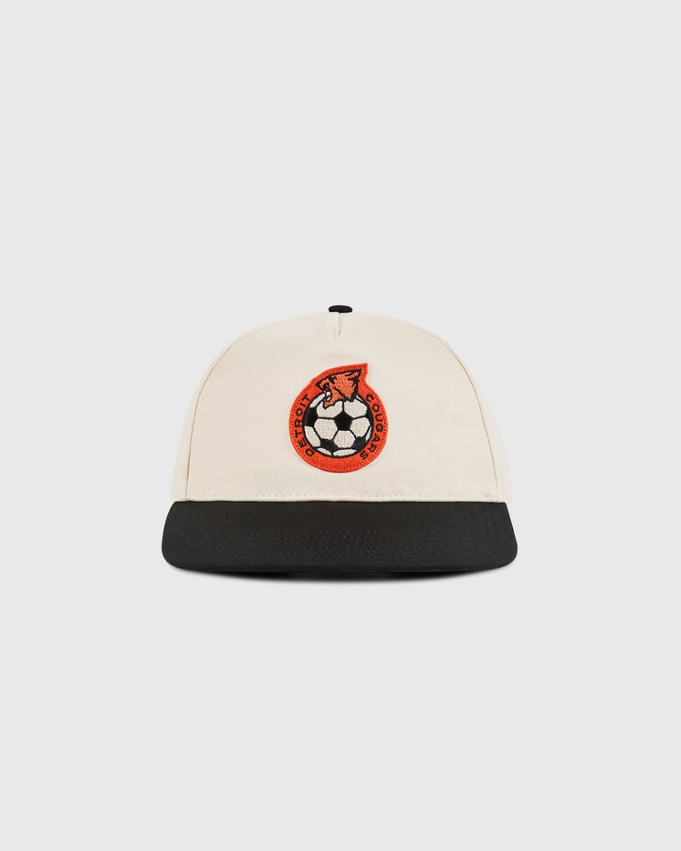 The Ebbets Field Detroit Cougars A-Frame Cotton Twill Ballcap, in beige with a black brim and an embroidered red and black soccer ball and horse's head emblem, is shown against a plain white background.