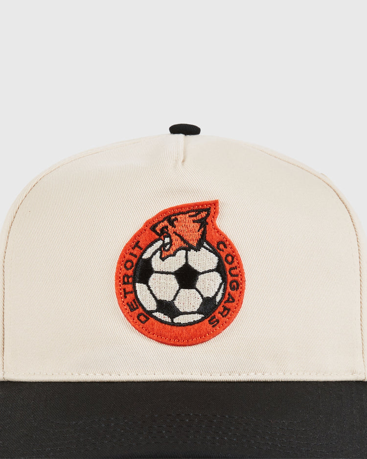 Close-up of the Detroit Cougars A-Frame Cotton Twill Ballcap by Ebbets Field, featuring a beige crown, black brim, and a red/black embroidered cougar with 