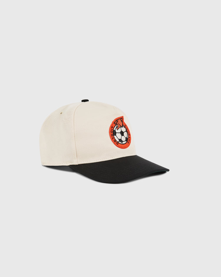 The Ebbets Field Detroit Cougars A-Frame Cotton Twill Ballcap features a beige crown, black brim, and an embroidered red and black soccer ball patch on the front, shown against a plain white background.
