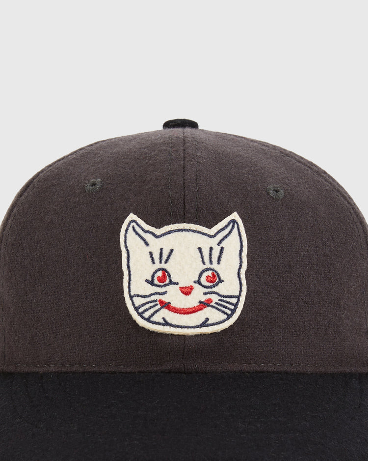 A close-up of the Ebbets Field Kansas City Katz 1961 Wool Ballcap in youth size—a black cap with an embroidered white cat face featuring red eyes, a red nose, and a smiling mouth on the front.