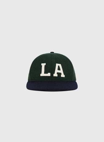 The Ebbets Field Los Angeles Angels (PCL) 1949 Wool Ballcap features a green crown, dark blue brim, and bold white LA letters on the front, echoing classic Pacific Coast League style, shown against a simple light background.