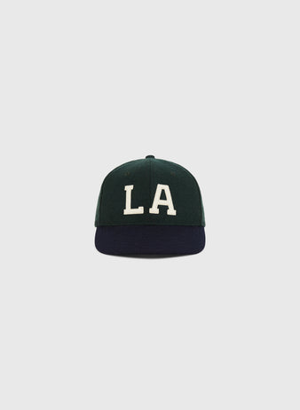 The Ebbets Field Los Angeles Angels (PCL) 1949 Wool Ballcap in youth size features a dark green crown, dark blue brim, and large white LA embroidery, shown against a light gray background.