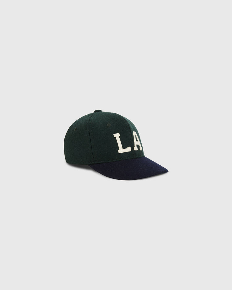 The Los Angeles Angels (PCL) 1949 Wool Ballcap for youth by Ebbets Field features dark green wool, a black brim, and bold white LA letters on the front, inspired by classic Pacific Coast League style, shown on a light gray background.