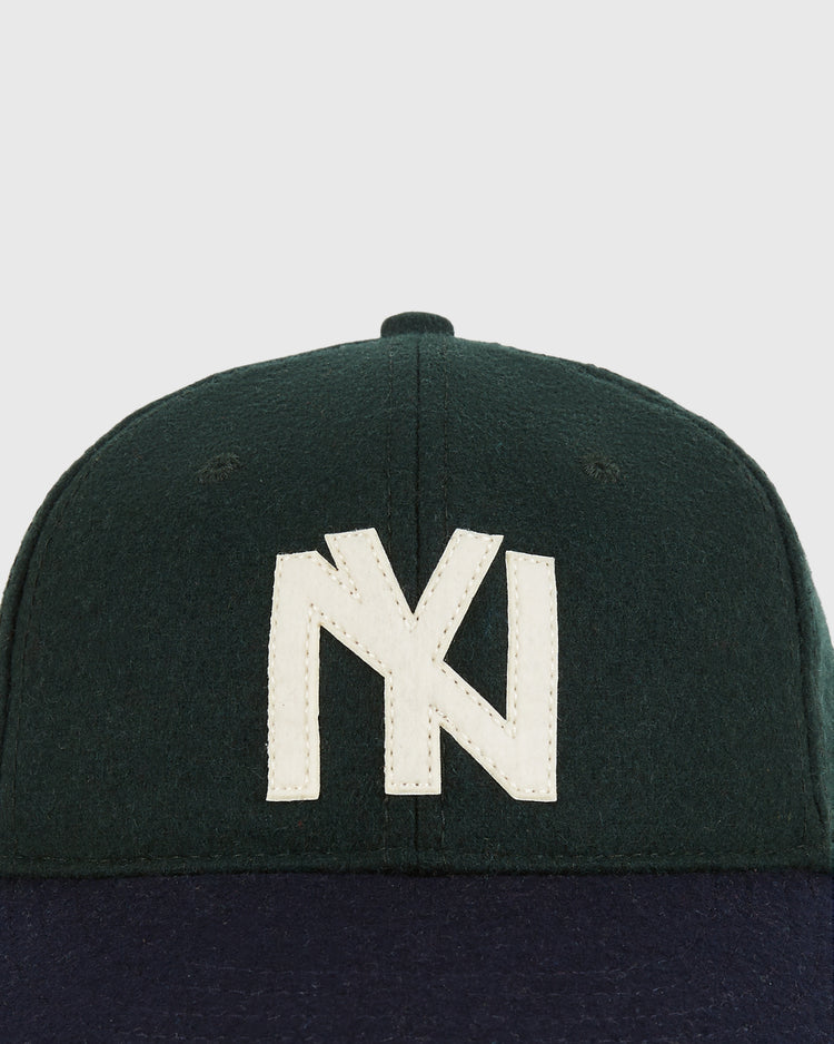 The BK Eagles 1935 Authentic Ballcap by Ebbets Field is a dark green cap with a navy blue brim and a large, white, stylized NY logo on the front.