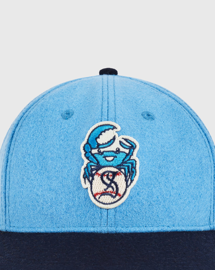 Close-up of the Ebbets Field Santurce Cangrejeros Crab Wool Ballcap in light blue with a navy brim, featuring an embroidered blue crab holding a baseball patch on the front—a tribute to Puerto Rican baseball heritage.