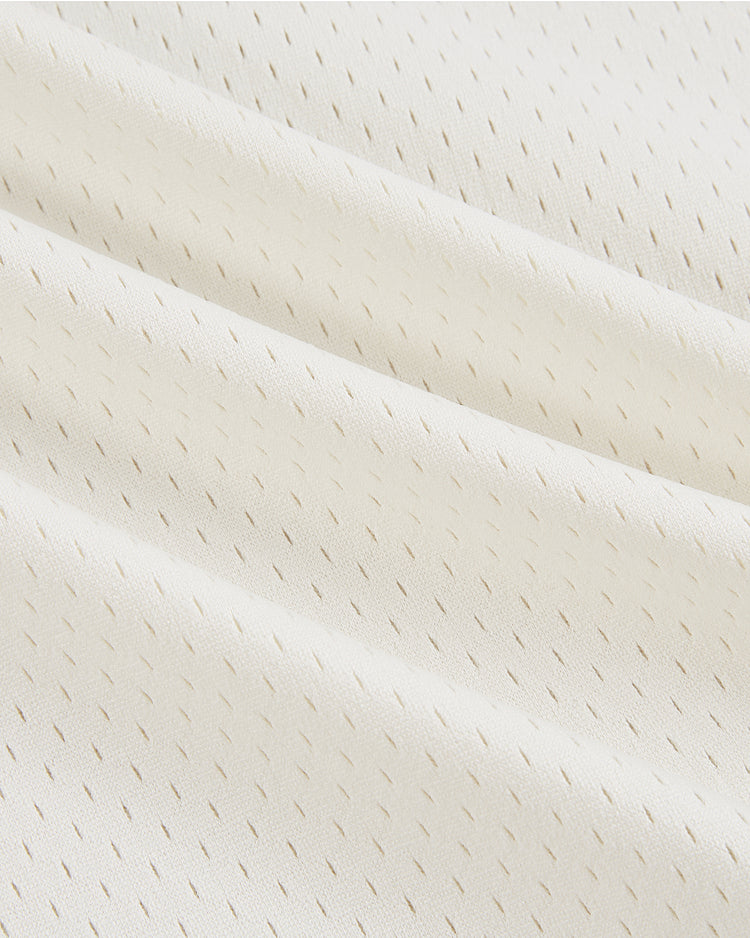 Close-up of white mesh fabric from the Ebbets Field Dallas Tornado Mesh Soccer Jersey, featuring a subtle pattern of small vertical perforations for breathability and texture. The material is softly folded in diagonal lines, reflecting vintage style.