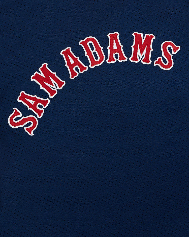 The Sam Adams Mesh V-Neck Jersey by Ebbets Field features a classic navy mesh design with “SAM ADAMS” in bold, arched white letters outlined in red, echoing vintage Ebbets Field team uniforms.