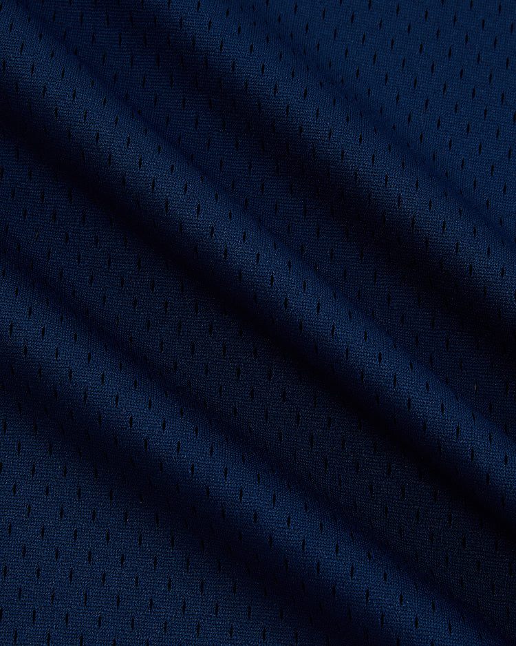 Close-up of dark blue athletic mesh fabric with small perforated holes and gentle folds, highlighting the breathable texture of the Sam Adams Mesh V-Neck Jersey by Ebbets Field.