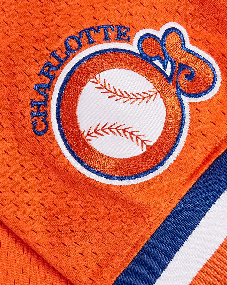Close-up of the Ebbets Field Cal Ripken Jr. Charlotte Orioles Mesh V-Neck Jersey, an orange mesh baseball jersey with CHARLOTTE and a baseball-themed logo, featuring blue and white trim at the bottom right—a style inspired by the classic Charlotte Orioles jersey.