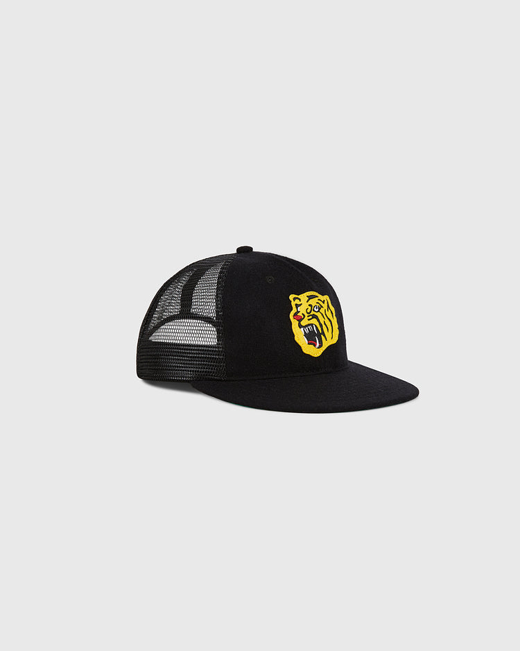 The Ebbets Field Osaka Tigers Wool Mesh Trucker Ballcap features a black mesh design and is accented with a yellow roaring lion patch on the front panel, displayed against a plain light gray background.