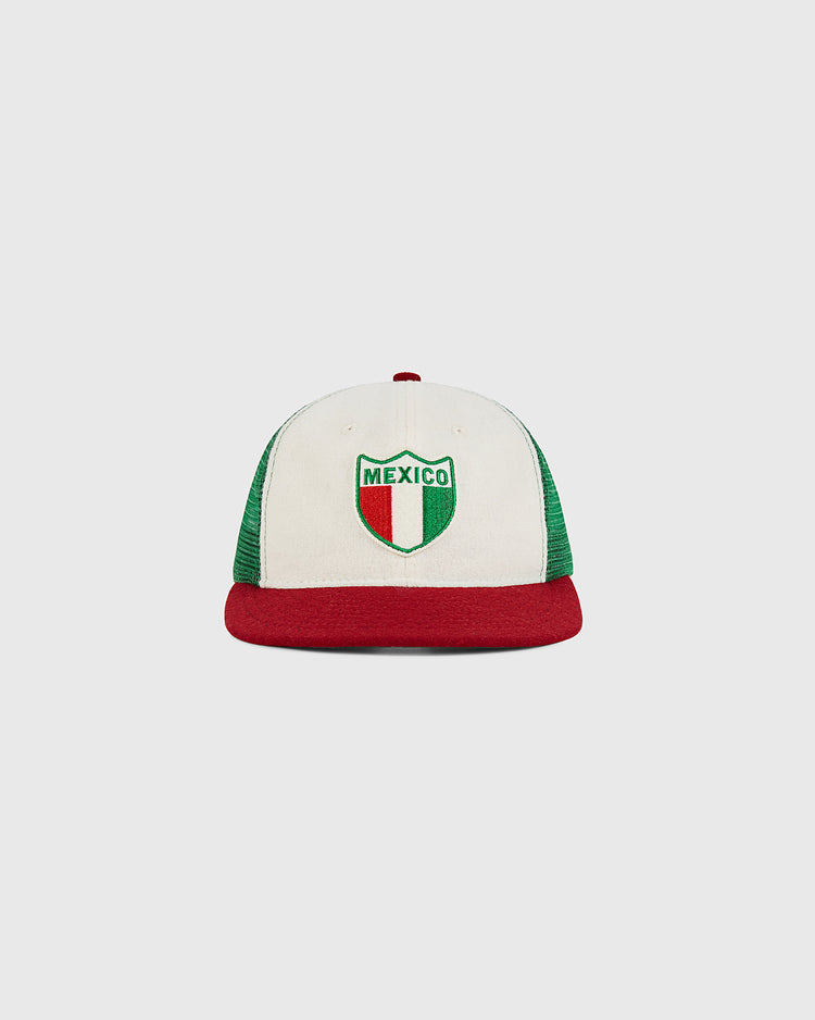 The Ebbets Field Mexico Wool Mesh Trucker Ballcap features a white and green design with a red brim and a Mexico crest on the front in green, white, and red—the colors of the Mexican flag.