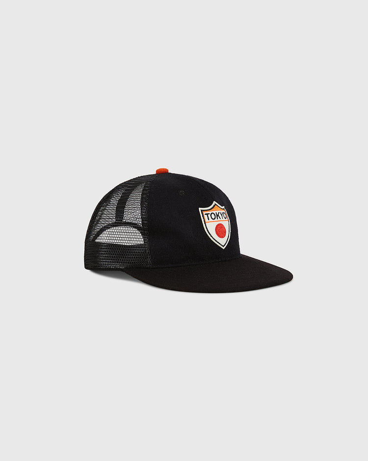 The Ebbets Field Tokyo Giants Wool Mesh Trucker Ballcap features a black wool construction, mesh panels, a flat brim, and an embroidered front patch that reads 