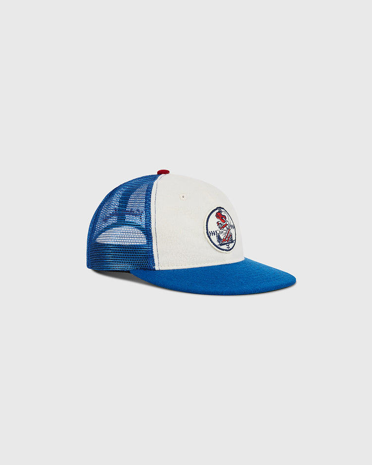 The Ebbets Field Nashville Sounds Mesh Trucker Ballcap features a blue and white design with a mesh back, a blue brim, and a red button on top. The front displays a circular patch with a colorful cartoon bird.