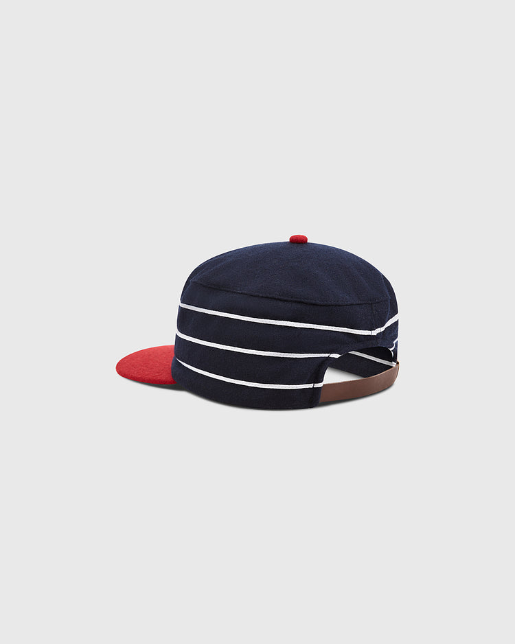 The Charleston Charlies Pillbox Cap by Ebbets Field features a navy blue retro design with white horizontal stripes, a red brim, and a small red button on top. An adjustable brown strap at the back ensures a comfortable fit.