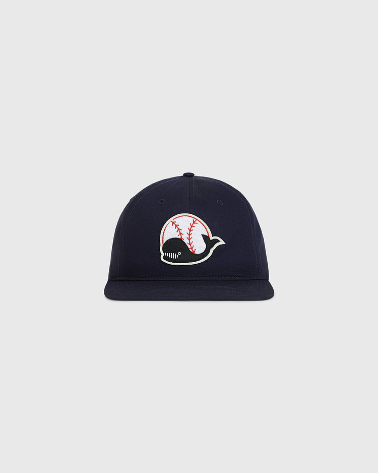 The Ebbets Field Taiyo Whales Cotton Twill Ballcap is a navy blue hat featuring a whale logo with baseball stitching on its body, displayed against a plain light gray background.