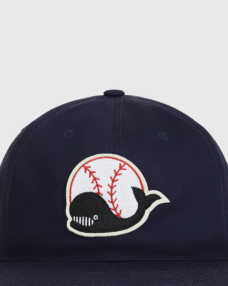 The Ebbets Field Taiyo Whales Cotton Twill Ballcap features a navy blue cotton twill construction and an embroidered logo of a smiling whale in front of a white baseball with red stitching, inspired by the classic Japanese baseball hat style and reminiscent of the original Taiyo Whales ballcap.