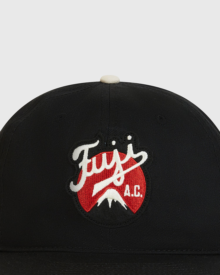 Introducing the Fuji Athletic Club Cotton Twill Ballcap by Ebbets Field—a classic black cotton twill cap adorned with an embroidered patch featuring “Fuji A.C.” text, a white mountain, and a red background. This design pays tribute to Japanese American baseball heritage and honors the legacy of the Fuji Athletic Club.
