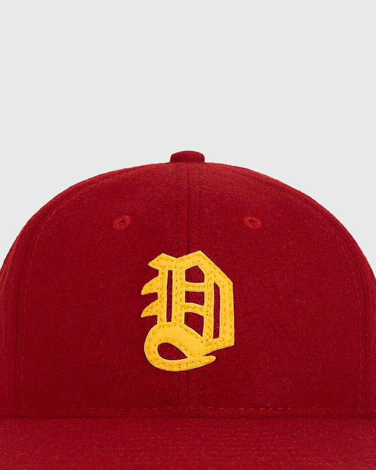 A close-up of the Daiei Stars 1949 Authentic Wool Ballcap by Ebbets Field, showcasing a yellow, stylized letter D embroidered on the front of a red cap against a plain light background. This genuine wool ballcap embodies the classic appeal of Japanese baseball memorabilia and pays tribute to the historic Daiei Stars.