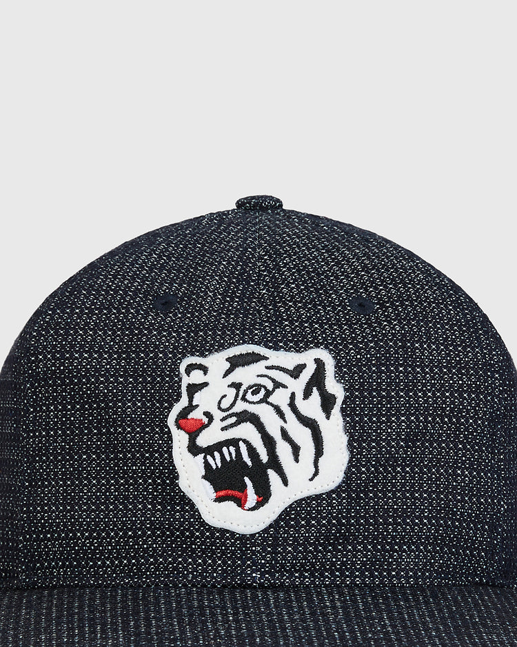 Introducing the Ebbets Field Osaka Tigers Japanese Indigo Cotton Dobby Ballcap—a navy indigo-dyed cap inspired by Japanese baseball, crafted from textured cotton dobby. The front showcases an embroidered patch featuring a white tiger’s head with black stripes, red accents, and an open mouth, paying homage to the legendary Osaka Tigers.