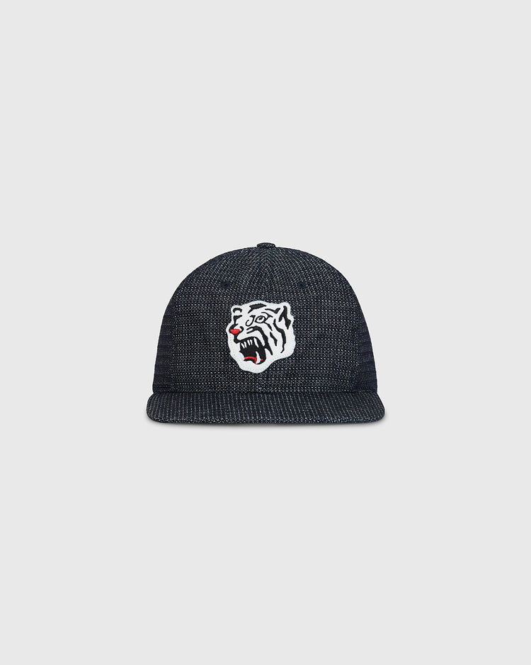 The Ebbets Field Osaka Tigers Japanese Indigo Cotton Dobby Ballcap is a dark, textured indigo-dyed cap featuring a white embroidered tiger head with black stripes and red accents on the front. Inspired by Japanese baseball and echoing the iconic Osaka Tigers, this ballcap is showcased against a plain light gray background.