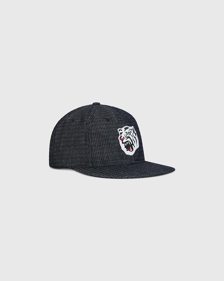 The Ebbets Field Osaka Tigers Japanese Indigo Cotton Dobby Ballcap is a dark, indigo-dyed cap crafted from dobby cotton, featuring an embroidered open-mouthed white tiger with a red tongue on the front—evoking classic Japanese baseball style and the spirit of the Osaka Tigers—shown against a plain light gray background.