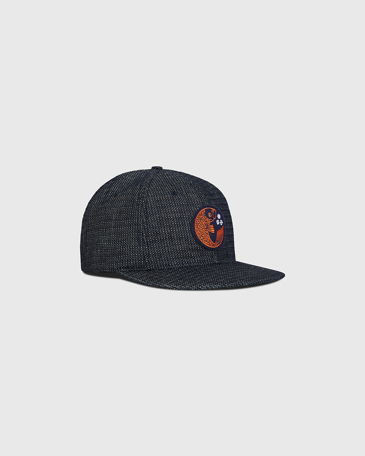 The Ebbets Field Hiroshima Carp Japanese Indigo Cotton Dobby Ballcap is a dark textured snapback with a curved brim, made from premium Japanese indigo cotton and adorned with an orange and white embroidered cat’s face patch on the front, shown against a plain light background.